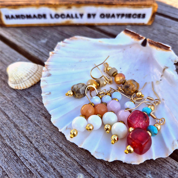 Colorful beaded earrings on a shell with 'Handmade Locally by Quay Pieces' sign in the background.