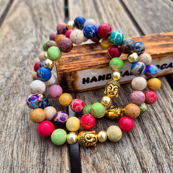 A set of colorful beaded bracelets with gold Buddha charms, displayed on a rustic wooden surface next to a wooden block.