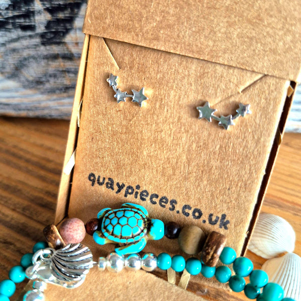 A close-up of jewelry displayed on a brown kraft card labeled 'quaypieces.co.