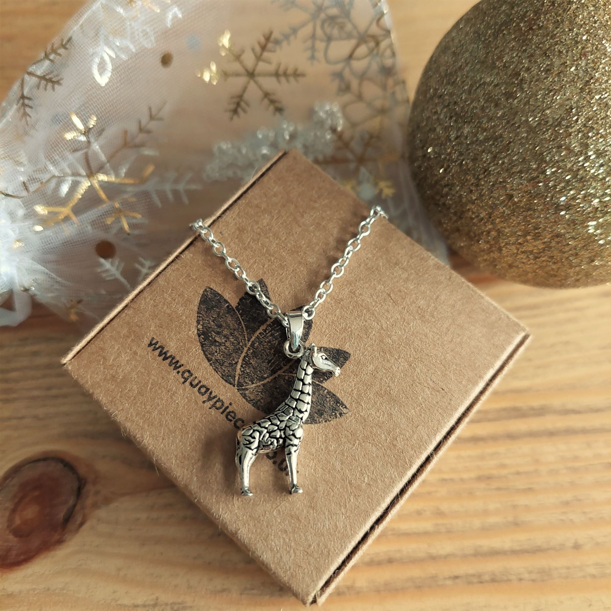 Silver giraffe necklace on a brown box with decorative background