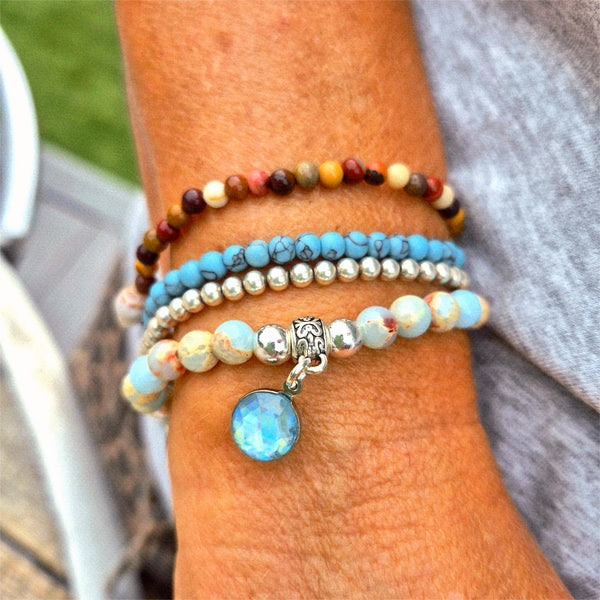 Close-up of a wrist wearing multiple beaded bracelets with a blue charm.