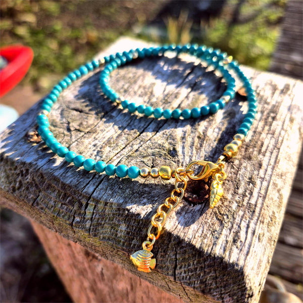 Turquoise beaded necklace with a gold chain on a wooden surface
