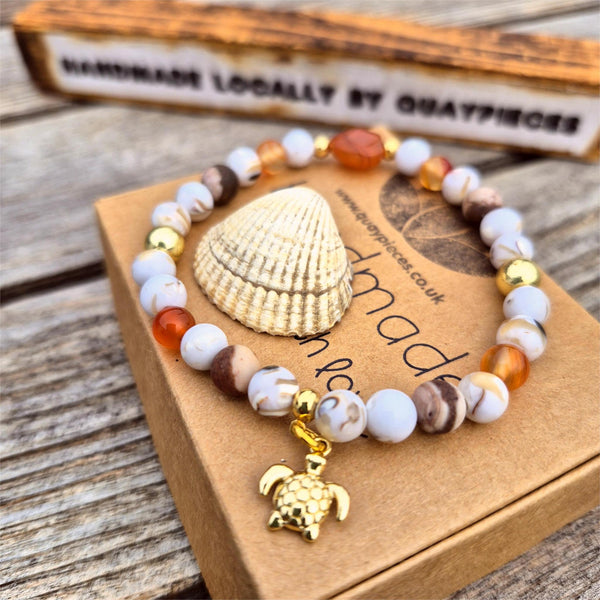 Beaded bracelet with a shell and turtle charm on a wooden surface
