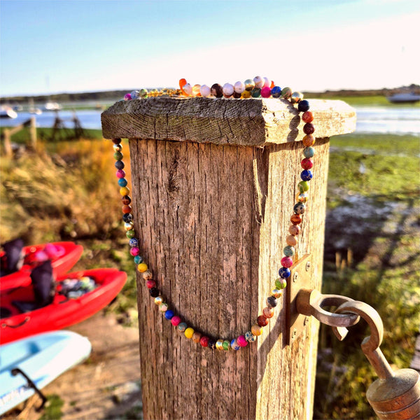 Colorful beaded necklace on a wooden post with kayaks and a lake in the background