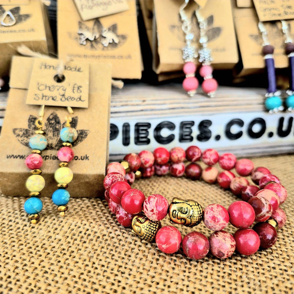 Colorful beaded bracelet with a gold Buddha charm on a textured surface with brand packaging in the background.