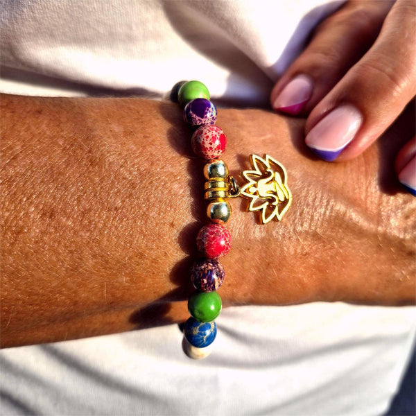 Colorful beaded bracelet with a gold leaf charm on a wrist against a white background