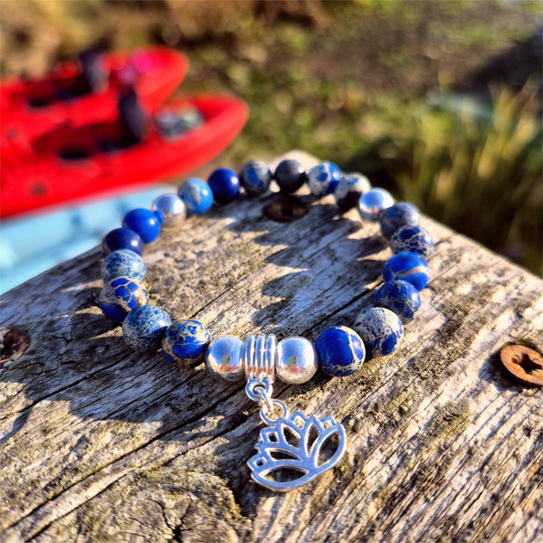 Beaded bracelet with a silver tree of life charm on a wooden surface with a blurred outdoor background