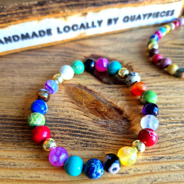 Colorful beaded bracelet on a wooden surface with 'Quaypieces' branding.