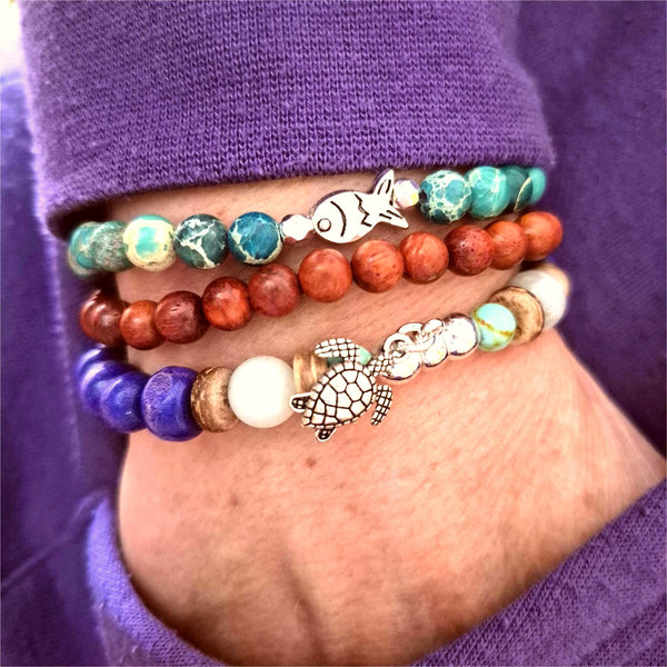 Discover three stunning handmade bracelets that work beautifully together. This vibrant trio features 8mm purple wood beads with coconut discs, aqua stone beads &amp; silver turtle (nickel free), 6mm waxed natural wood beads paired with 6mm green imperial jasper beads with cute silver plated fish.